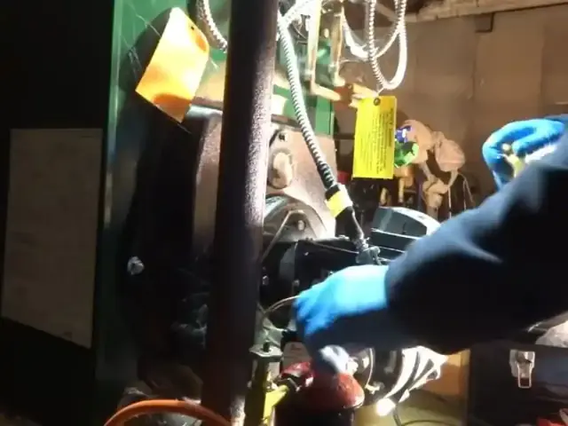 Gloved hands working on boiler pump and piping with a service tag attached