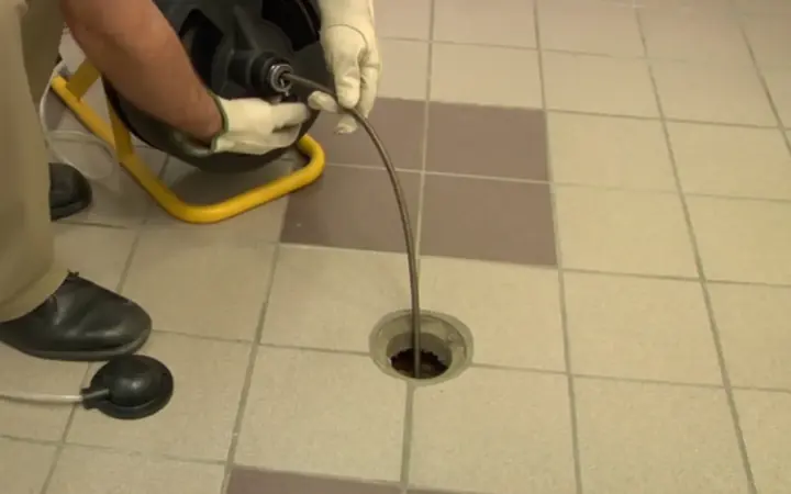 Technician feeding a drain snake cable into a floor drain set in tile