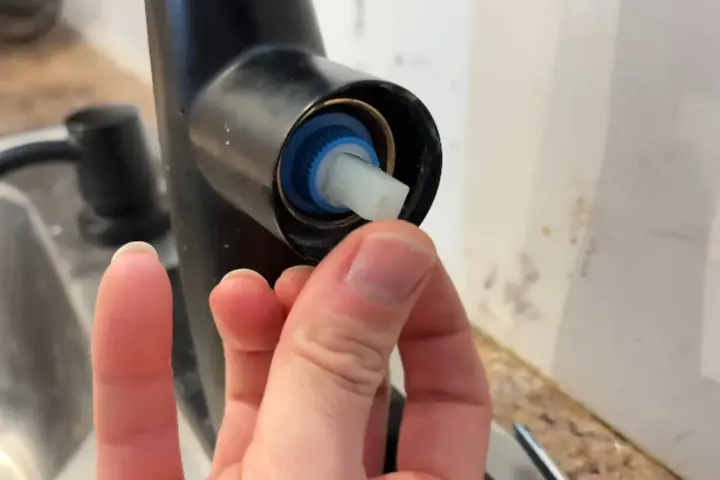 Hand holding a faucet cartridge removed from a kitchen faucet