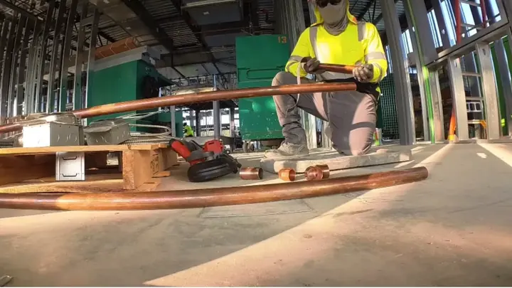 Plumber kneeling beside long runs of copper pipe inside a building under construction
