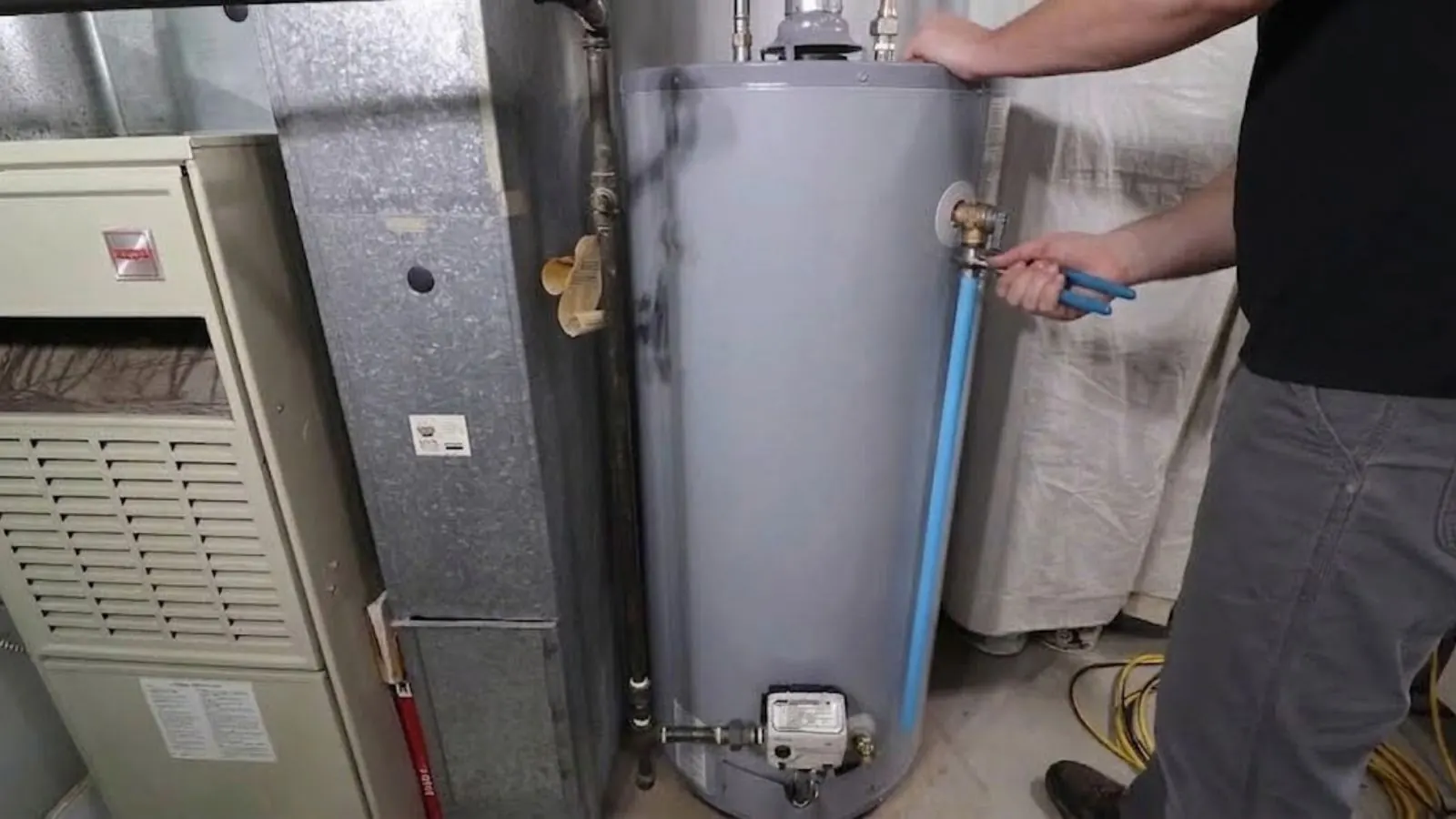 Technician's hand at the connections of a gas water heater next to a furnace