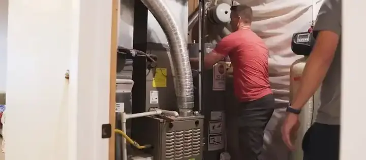 Two technicians working beside a water heater and furnace in a utility room